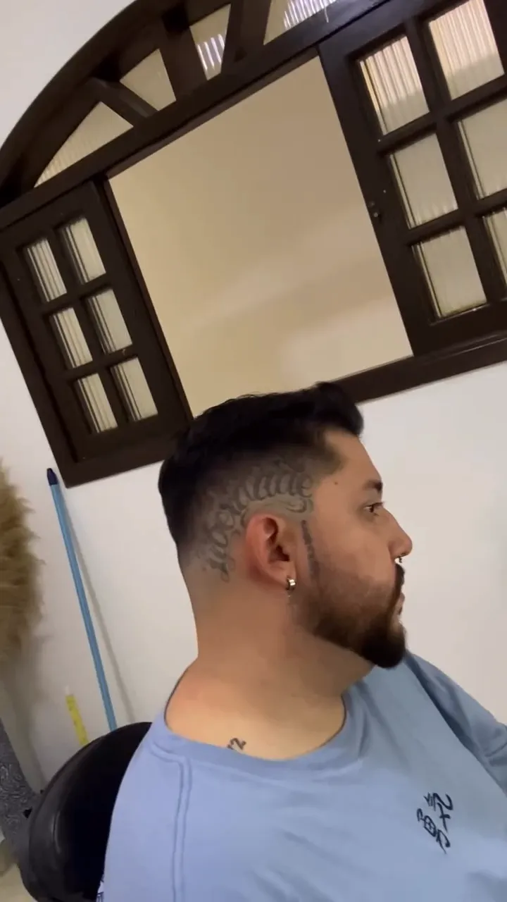 Cliente de barba cheia com degradê e um desenho na lateral da cabeça