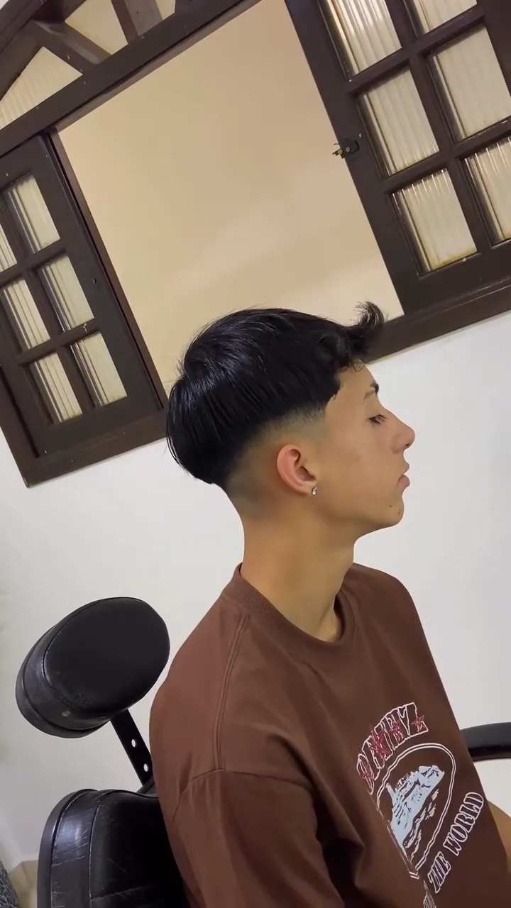Jovem de perfil com franja e degradê médio nas laterais
