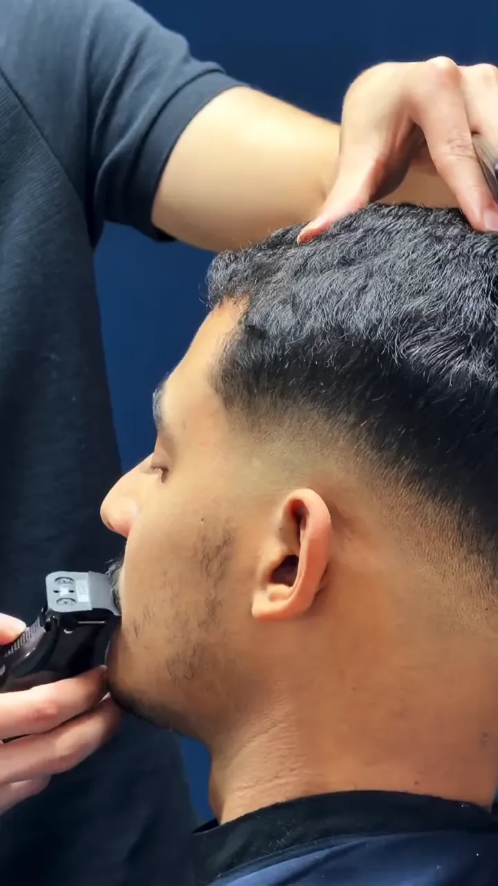 De perto: o barbeiro segura o cabelo do cliente e acerta a barba na máquina, com o degradê baixo já pronto